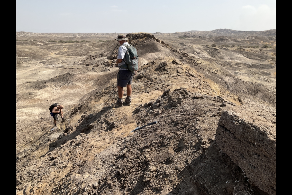 Two men observe the ground in an area of rugged terrain.